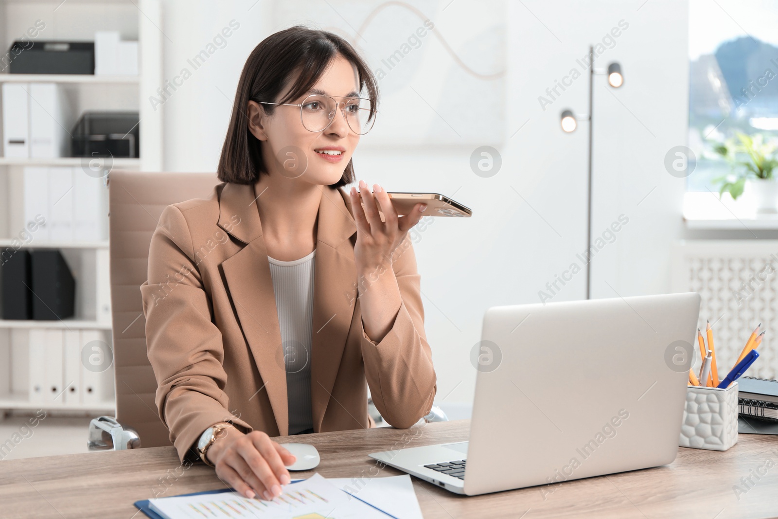 Photo of Beautiful woman recording voice message via smartphone in office