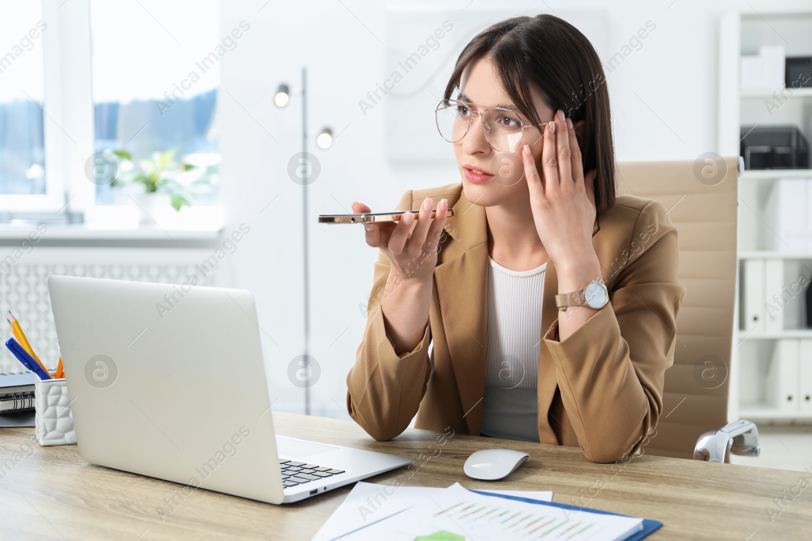 Photo of Beautiful woman recording voice message via smartphone in office