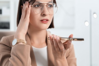 Beautiful woman recording voice message via smartphone in office, selective focus