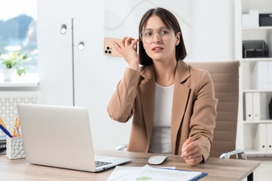 Beautiful woman with smartphone listening to voice message in office