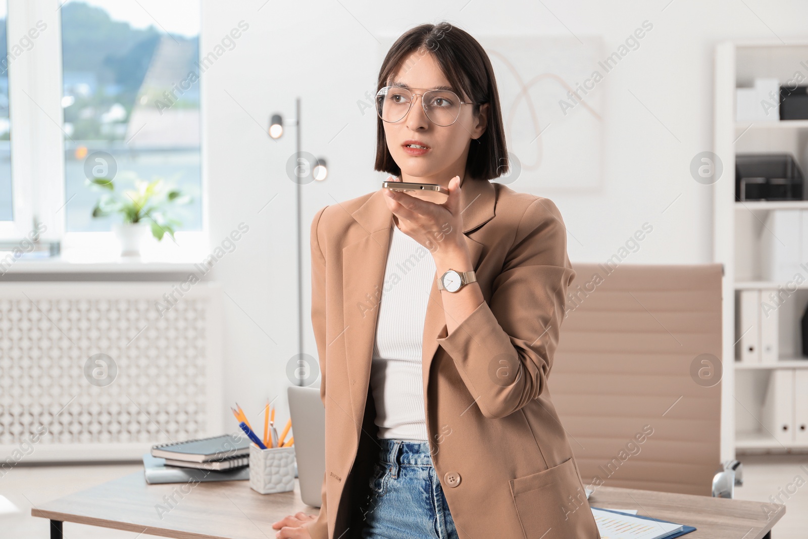 Photo of Beautiful woman recording voice message via smartphone in office