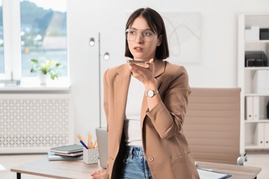 Beautiful woman recording voice message via smartphone in office