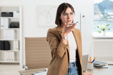 Photo of Beautiful woman recording voice message via smartphone in office