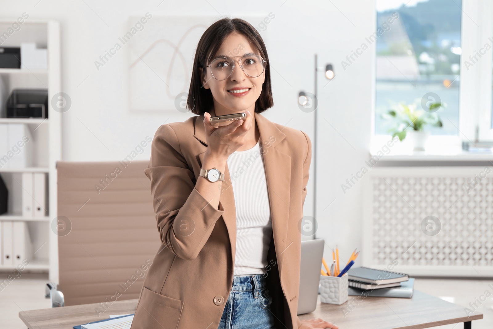 Photo of Beautiful woman recording voice message via smartphone in office