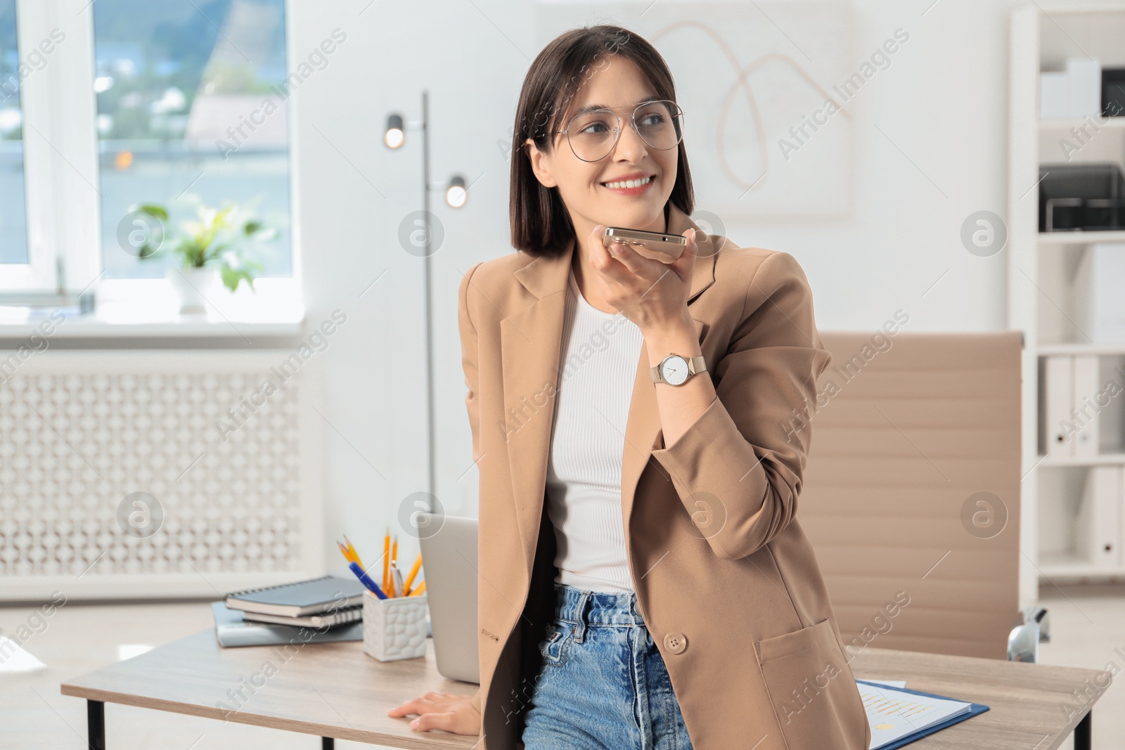 Photo of Beautiful woman recording voice message via smartphone in office