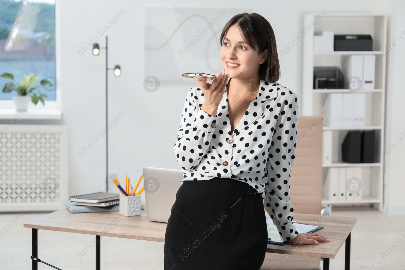 Photo of Beautiful woman recording voice message via smartphone in office