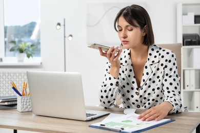 Photo of Beautiful woman recording voice message via smartphone in office