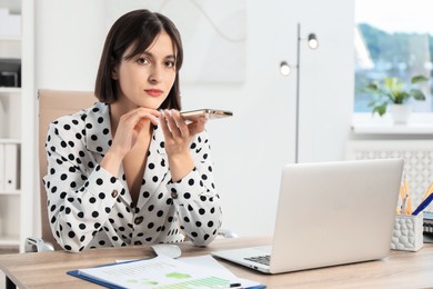 Photo of Beautiful woman recording voice message via smartphone in office