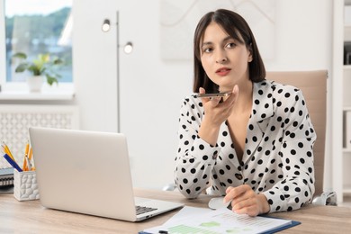 Photo of Beautiful woman recording voice message via smartphone in office