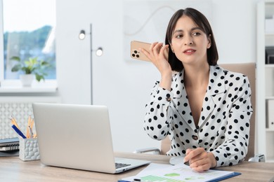 Beautiful woman with smartphone listening to voice message in office