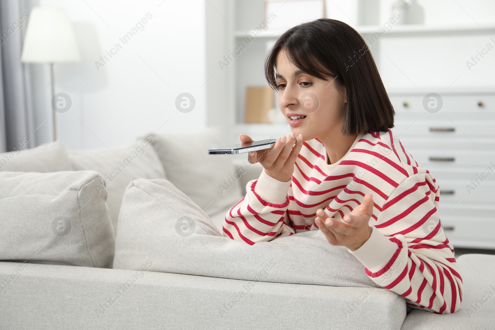 Photo of Beautiful woman recording voice message via smartphone at home