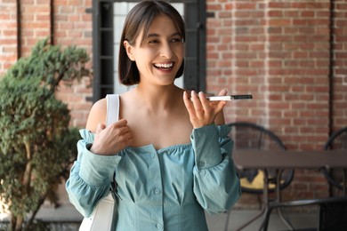 Photo of Beautiful woman recording voice message via smartphone outdoors