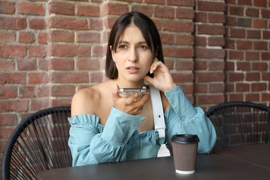 Photo of Beautiful woman recording voice message via smartphone in outdoors cafe