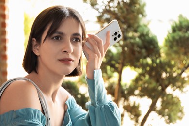 Photo of Beautiful woman with smartphone listening to voice message outdoors