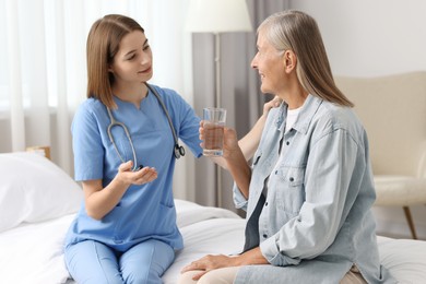 Young healthcare worker consulting senior patient on bed indoors