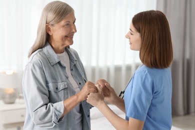 Photo of Young healthcare worker supporting senior patient indoors