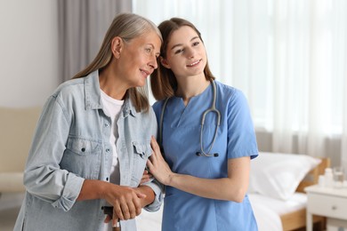 Photo of Smiling healthcare worker supporting senior patient indoors. Space for text