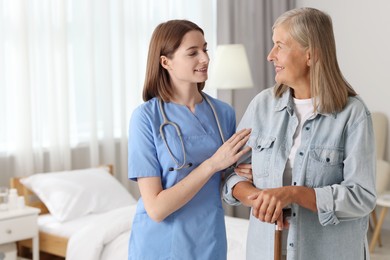 Smiling healthcare worker supporting senior patient indoors. Space for text