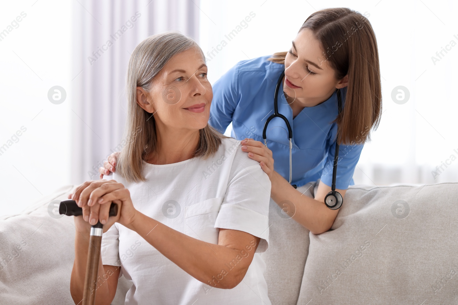 Photo of Young healthcare worker supporting senior patient indoors