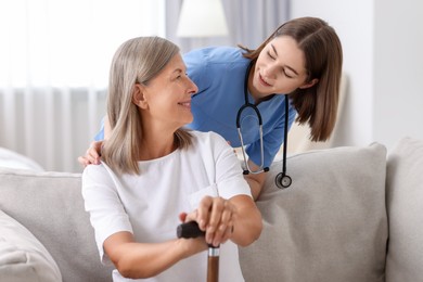 Photo of Smiling healthcare worker supporting senior patient indoors