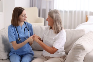 Photo of Smiling healthcare worker supporting senior patient indoors