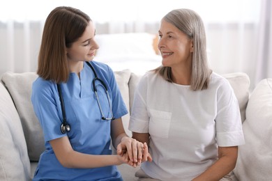 Photo of Young healthcare worker supporting senior patient indoors