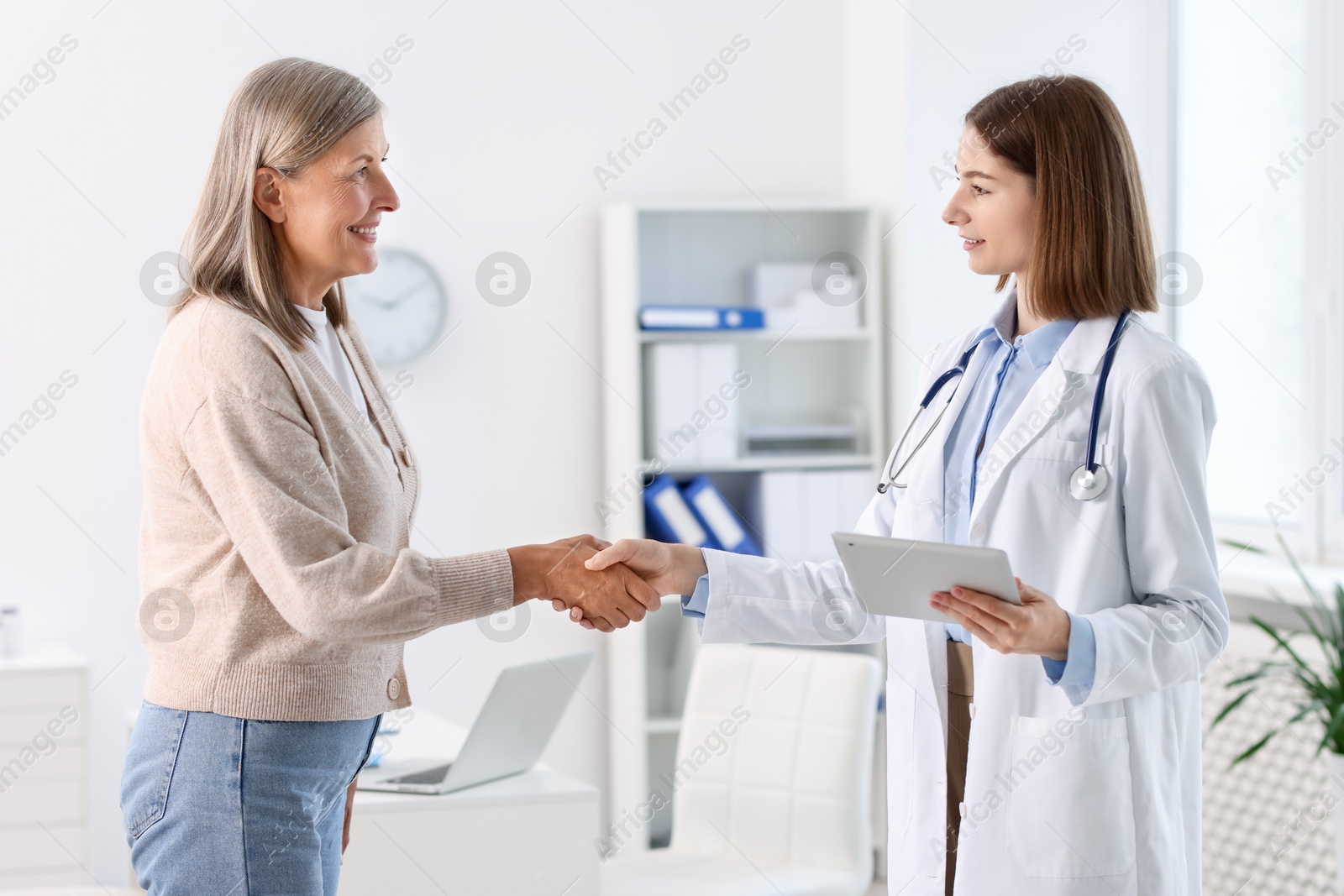 Photo of Smiling healthcare worker shaking hands with senior patient in hospital