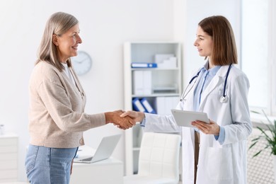 Smiling healthcare worker shaking hands with senior patient in hospital