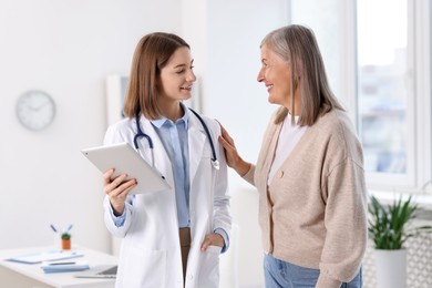 Photo of Smiling healthcare worker with tablet consulting senior patient in hospital