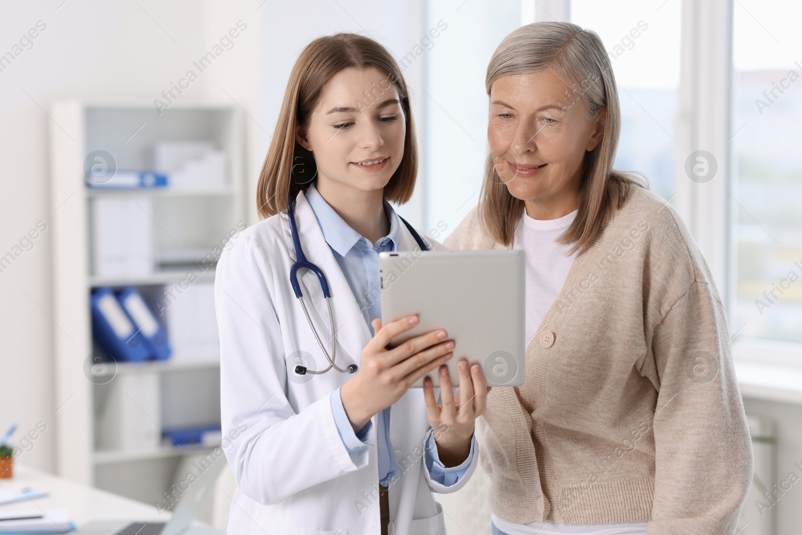 Photo of Smiling healthcare worker and senior patient checking analysis results on tablet in hospital