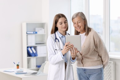 Smiling healthcare worker and senior patient checking analysis results on tablet in hospital. Space for text