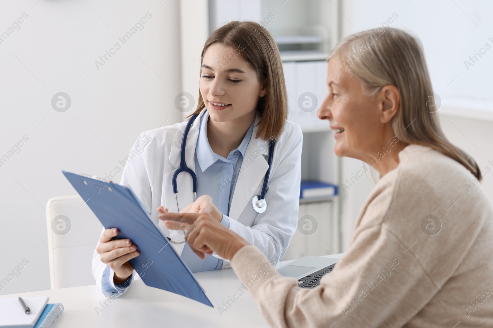 Photo of Smiling healthcare worker and senior patient checking clipboard with analysis results in hospital