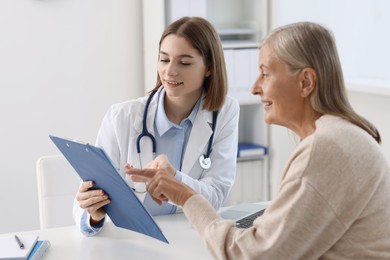 Smiling healthcare worker and senior patient checking clipboard with analysis results in hospital