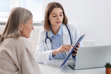 Photo of Healthcare worker and senior patient checking clipboard with analysis results in hospital