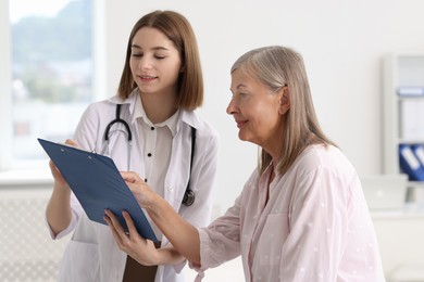 Photo of Smiling healthcare worker with clipboard consulting senior patient in hospital