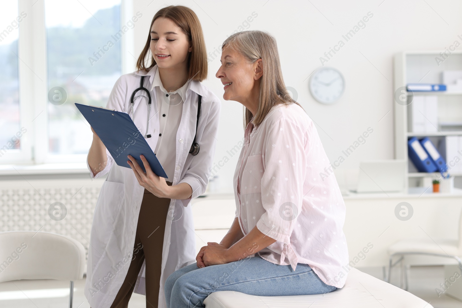 Photo of Smiling healthcare worker with clipboard consulting senior patient in hospital