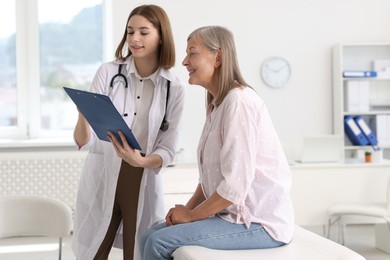 Smiling healthcare worker with clipboard consulting senior patient in hospital