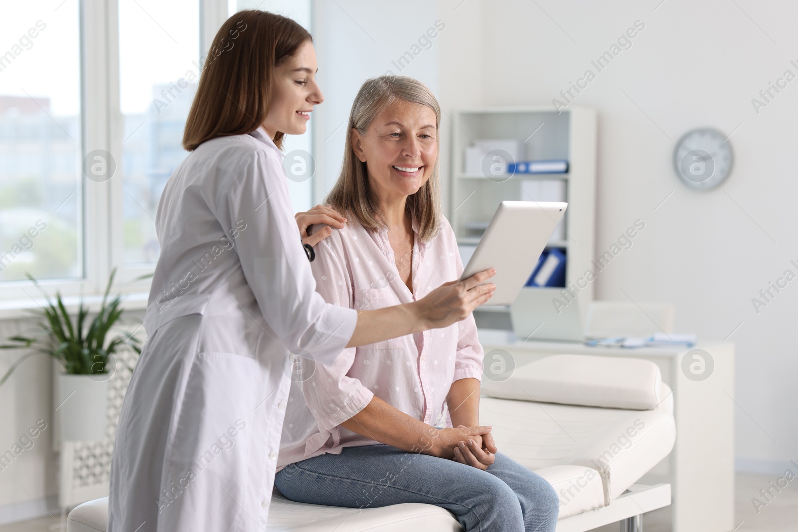 Photo of Smiling healthcare worker and senior patient checking analysis results on tablet in hospital