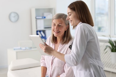 Smiling healthcare worker and senior patient checking analysis results on tablet in hospital