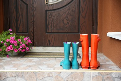 Photo of Two pairs of rubber boots on doorstep near entrance outdoors