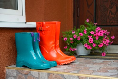 Photo of Two pairs of rubber boots on doorstep near entrance outdoors