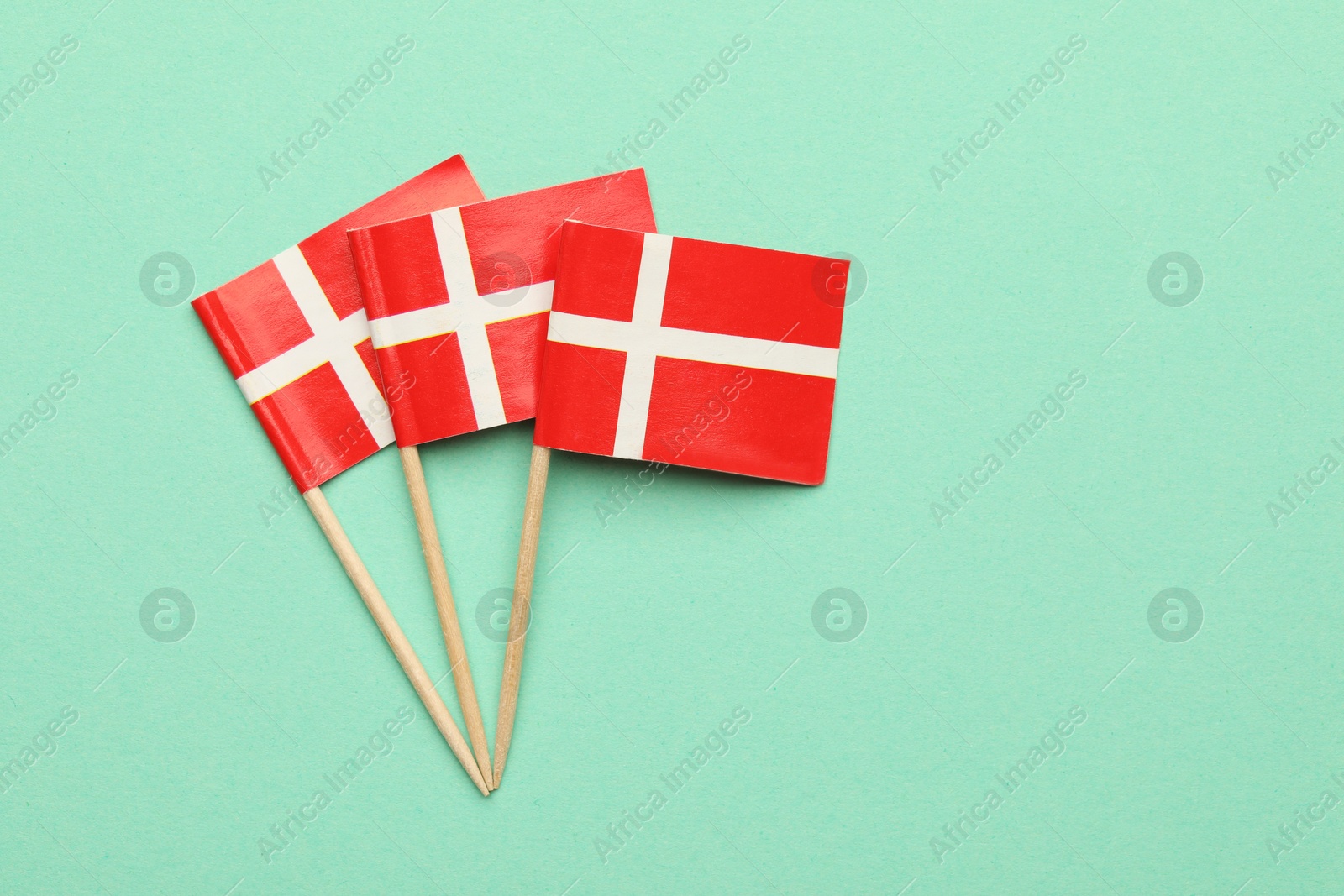 Photo of Small paper flags of Denmark on turquoise background, top view. Space for text