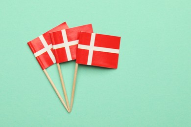 Photo of Small paper flags of Denmark on turquoise background, top view. Space for text