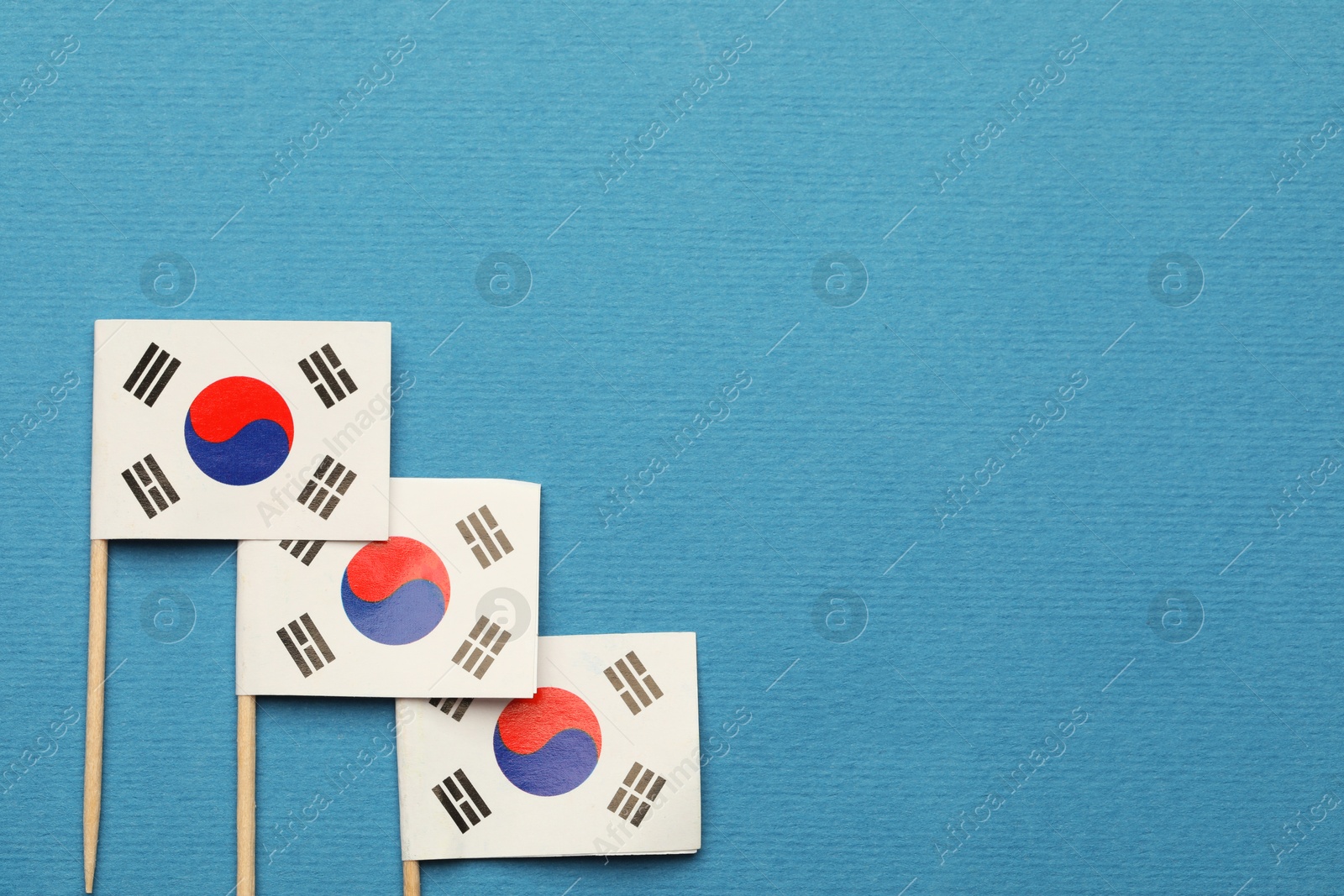 Photo of Small paper flags South Korea on light blue background, top view. Space for text