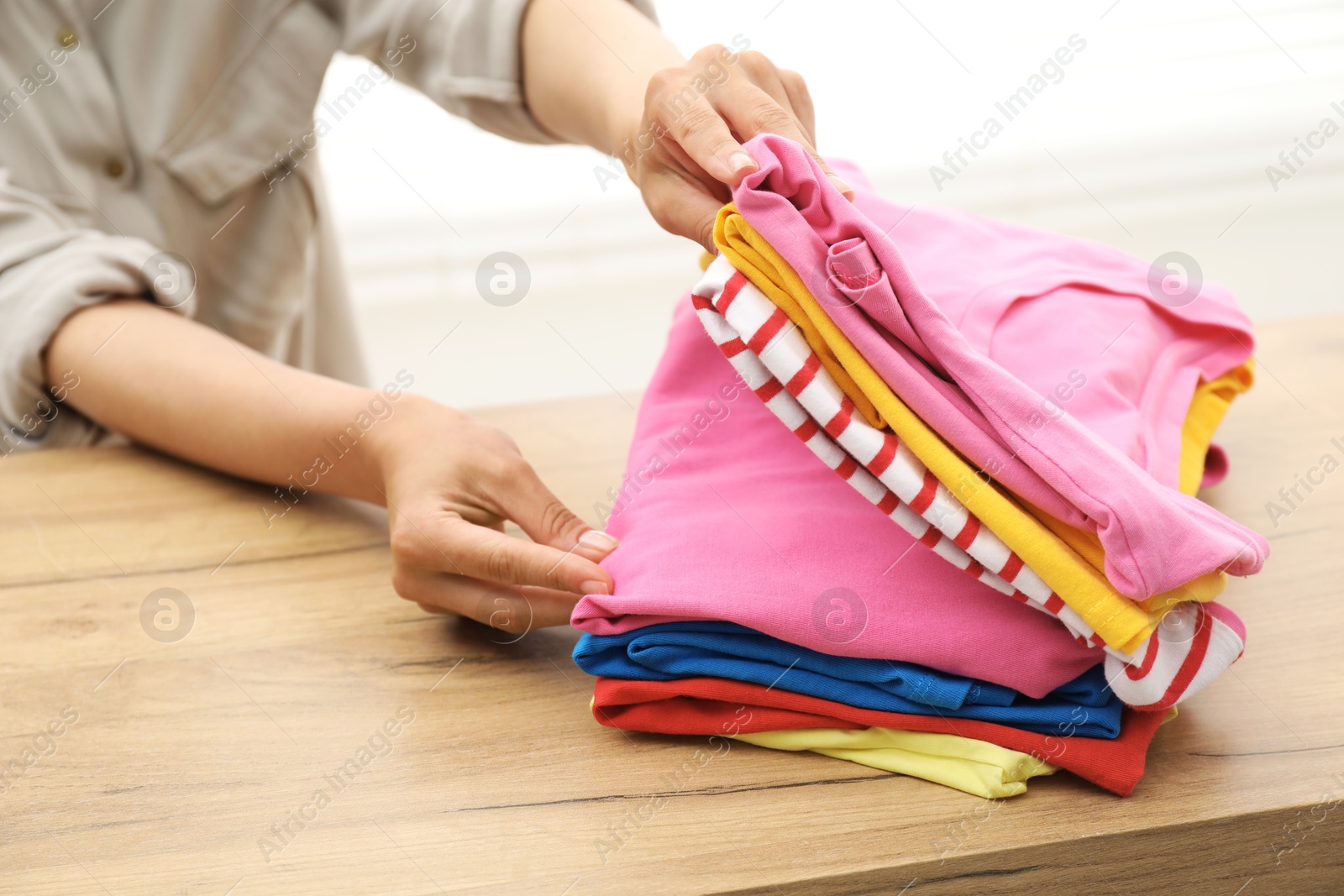 Photo of Woman stacking clean clothes at wooden table indoors, closeup