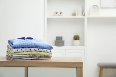 Photo of Stack of clean clothes on wooden dresser indoors