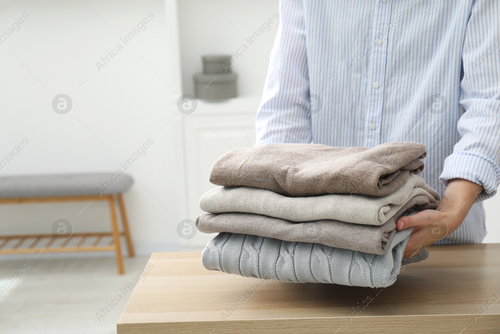 Photo of Woman with stack of clean clothes at wooden table indoors, closeup