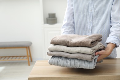 Photo of Woman with stack of clean clothes at wooden table indoors, closeup