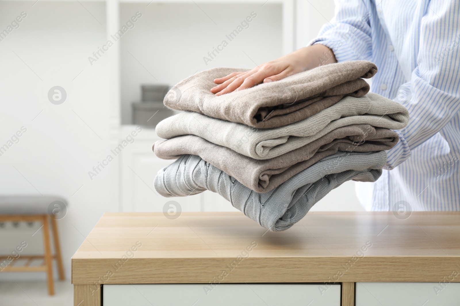 Photo of Woman with stack of clean clothes near wooden dresser indoors, closeup