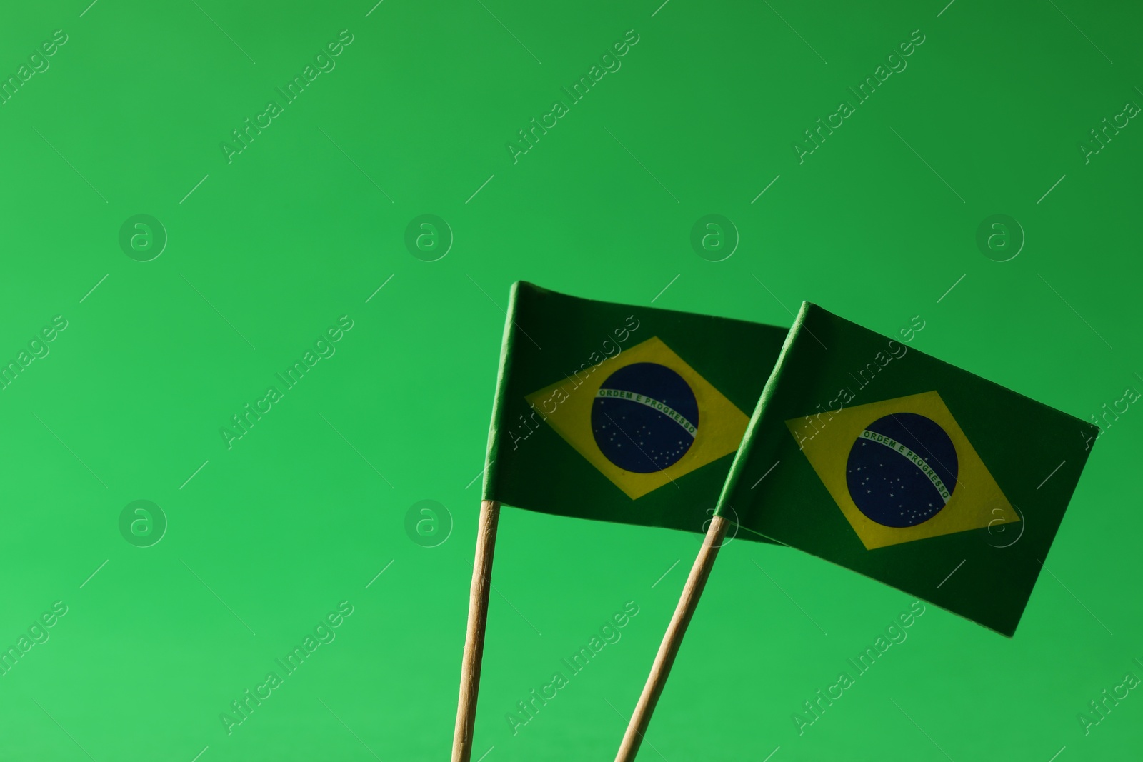 Photo of Small paper flags of Brazil on green background, space for text